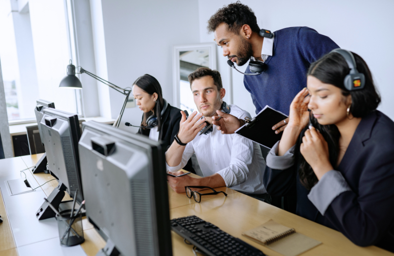 An outsourced IT specialist is assisting people that are working with a computer. Increased demand for help desk is one of the expected IT outsourcing trends.