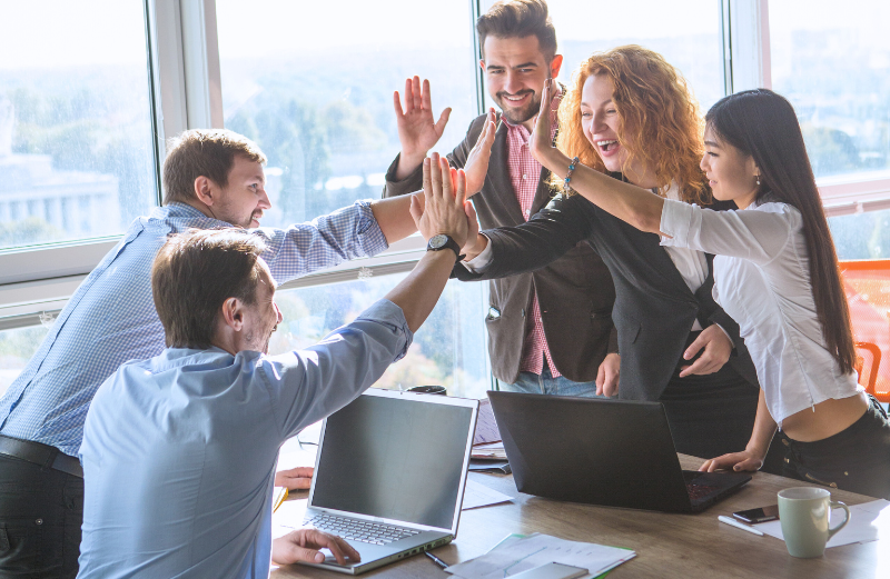 Team members high-fiving each other. Since teamwork, not office presence, is the key to productivity, company management can allow staff to take a workation.