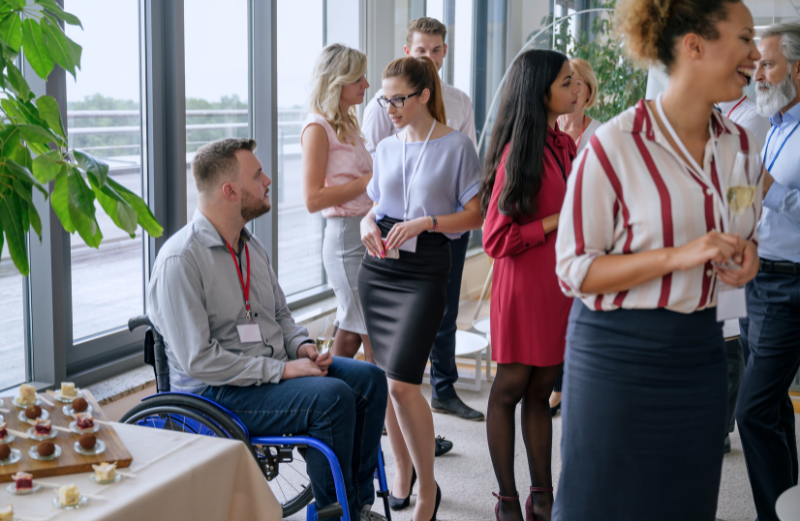 A man in a wheelchair talks with a colleague during a company party. Companies can encourage collaboration among employee support networks to foster an intersectional approach to diversity.